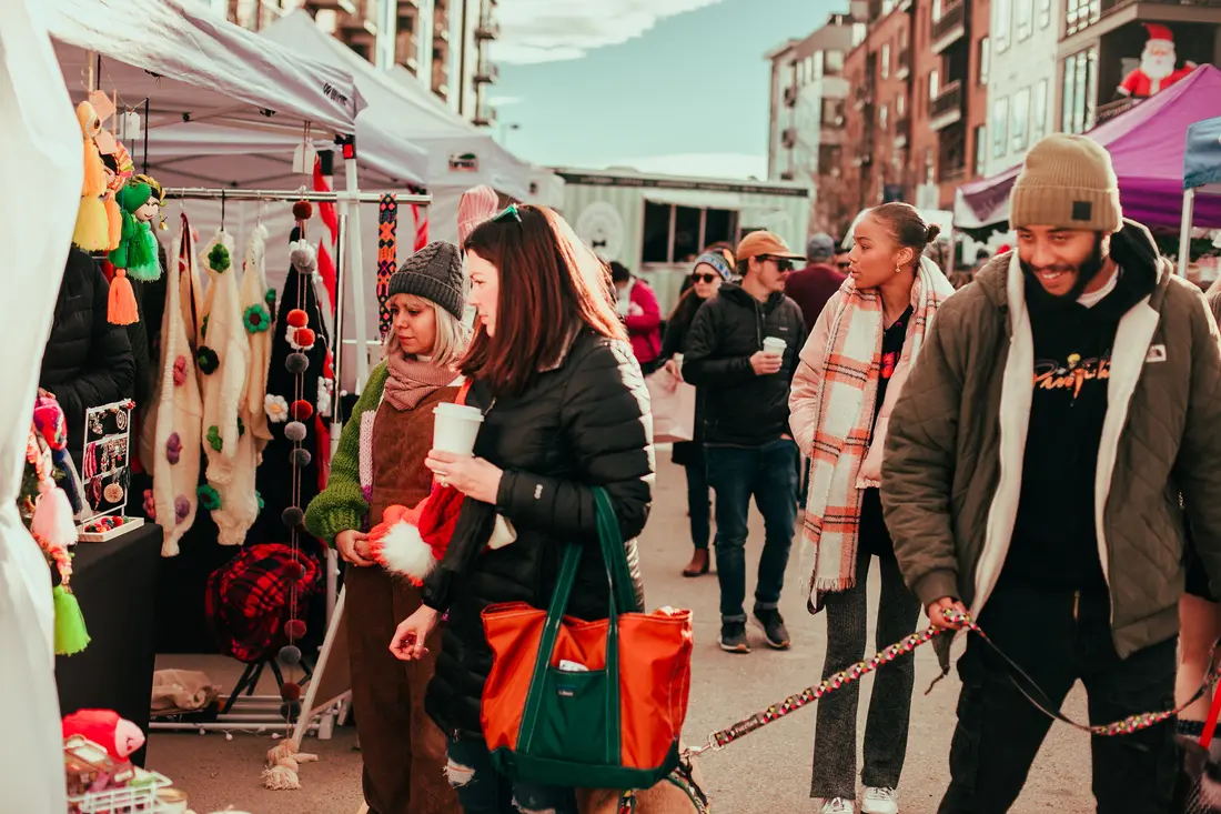 A couple with their dog and tote bags between the tents at the Belleview Station Holiday BAZAAR.
