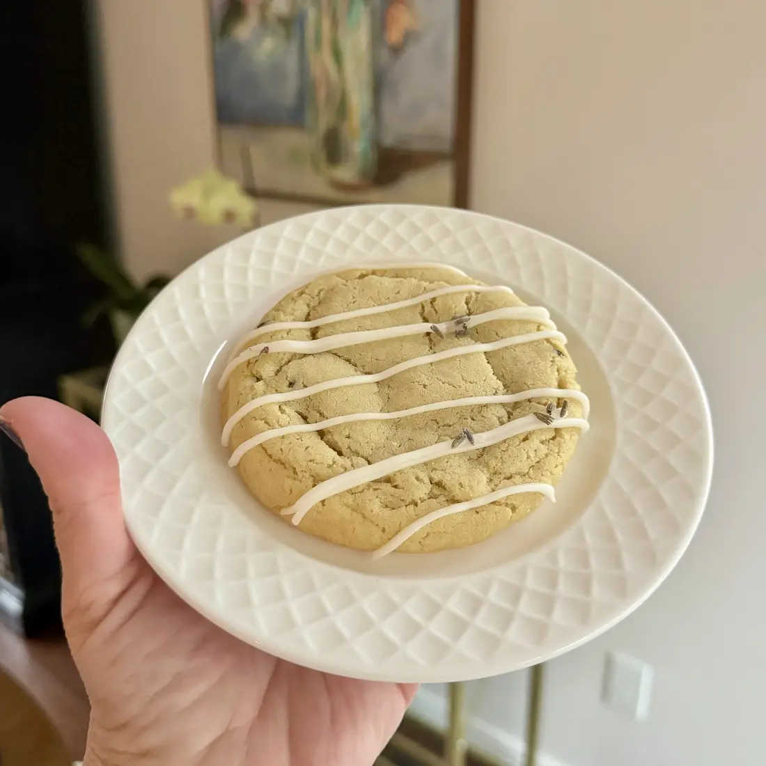 A hand holding a plate with a thick cookie striped in white icing.
