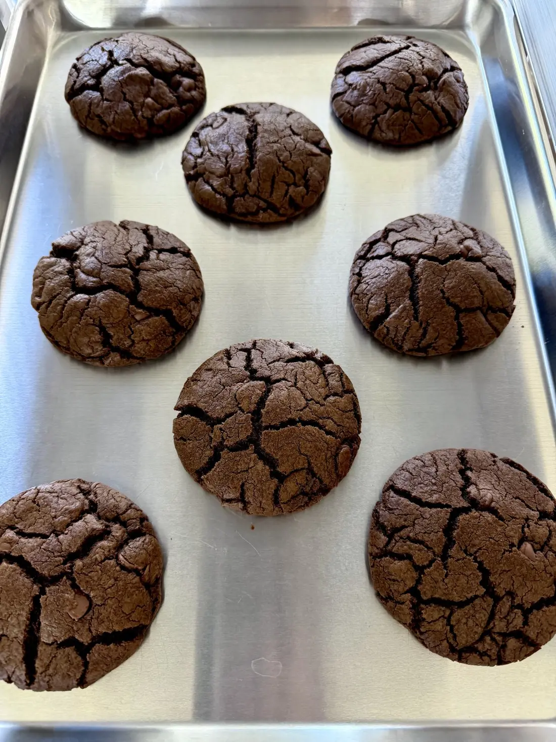 Six dark, cracked-top cookies on a baking tray.