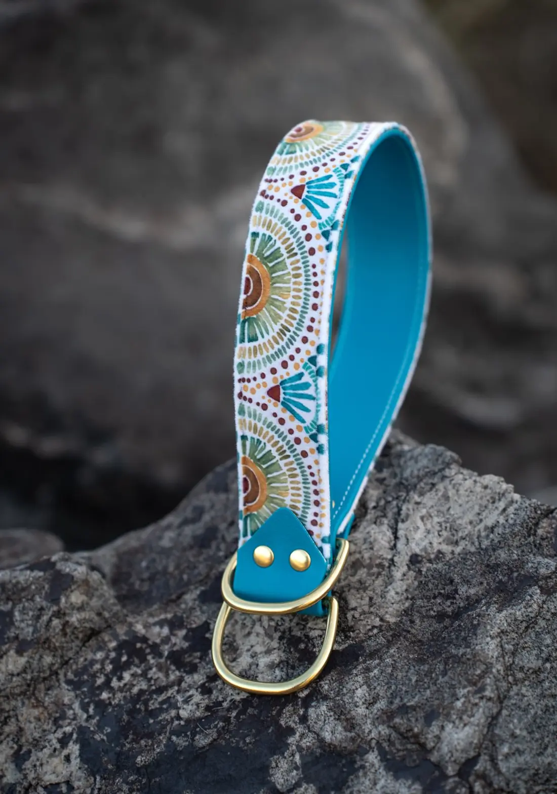 A blue patterned dog collar with a brass ring set on a rock.