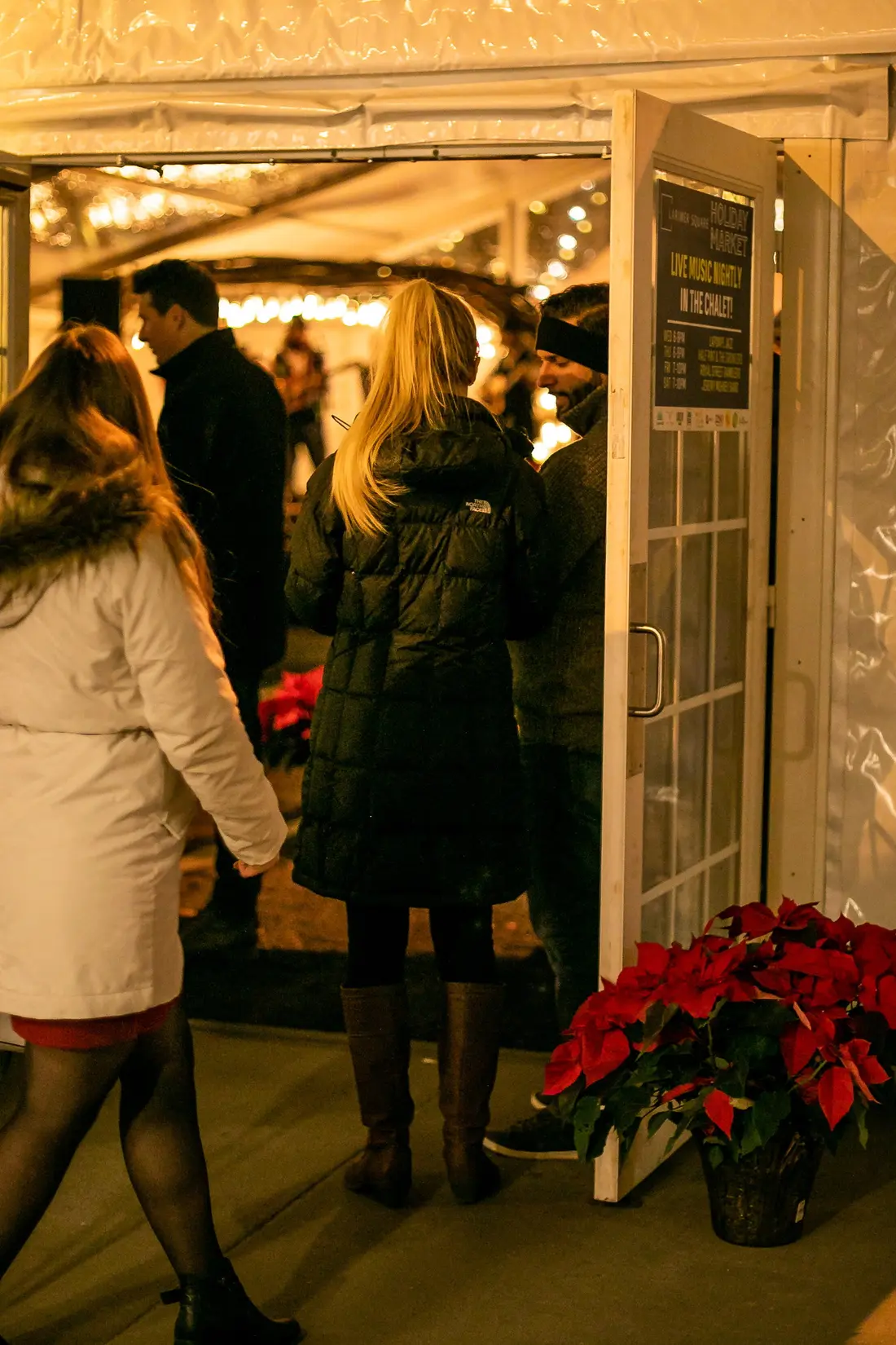 A couple stepping into a lit tent past a bank of red poinsettias.