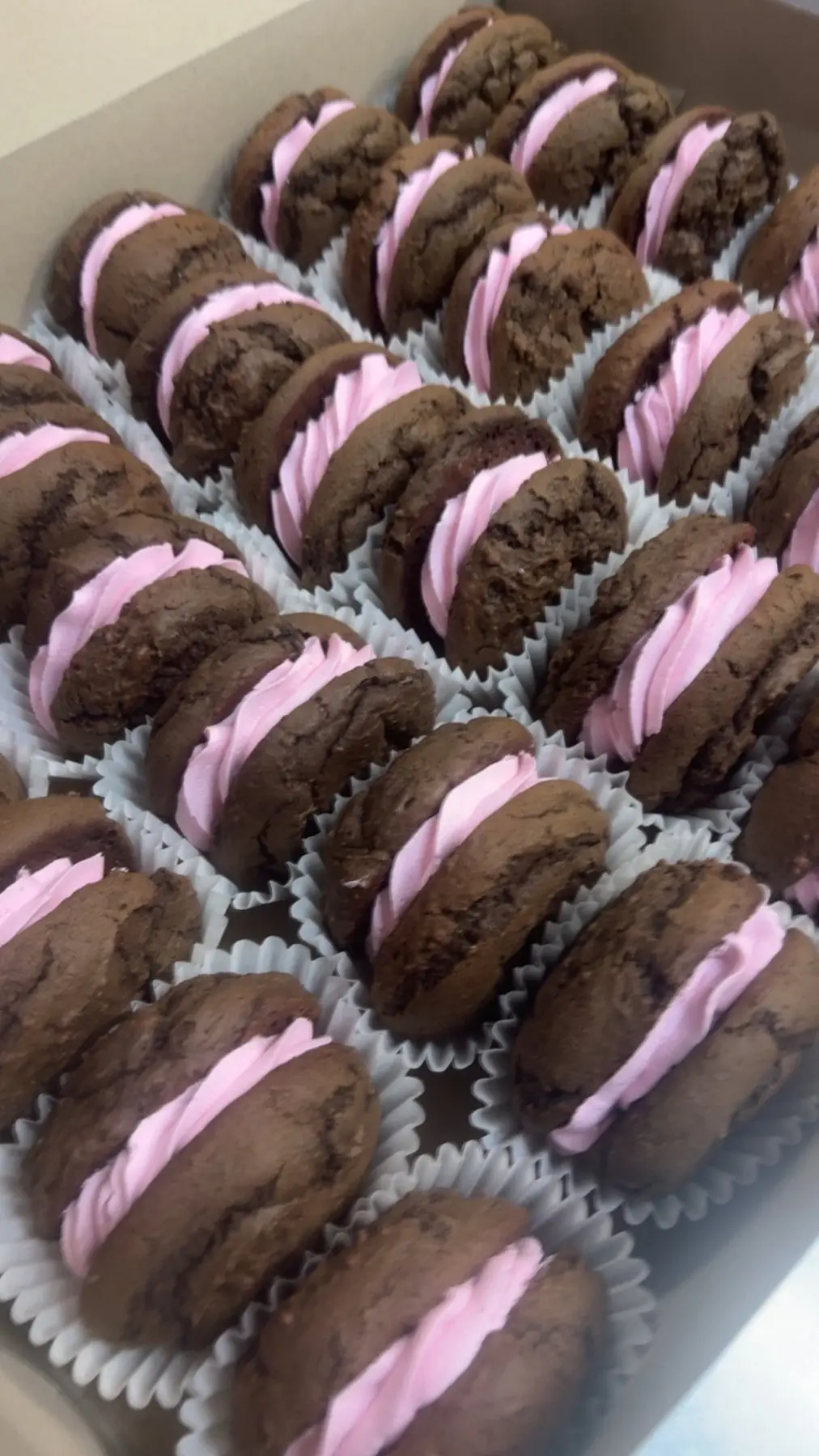 Rows of chocolate sandwich cookies with pink filling in paper cups.