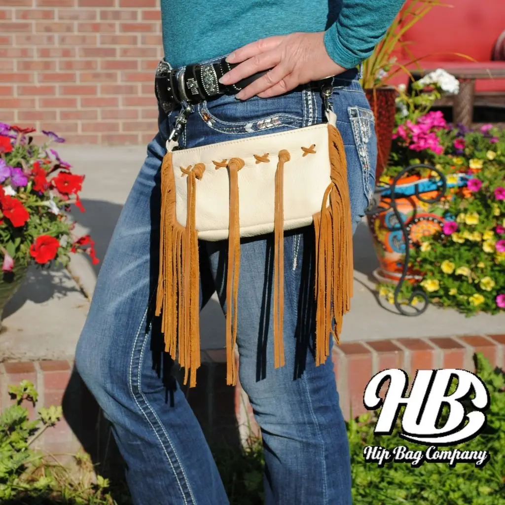 A cream leather hip bag with long fringe worn on the hip over blue jeans.