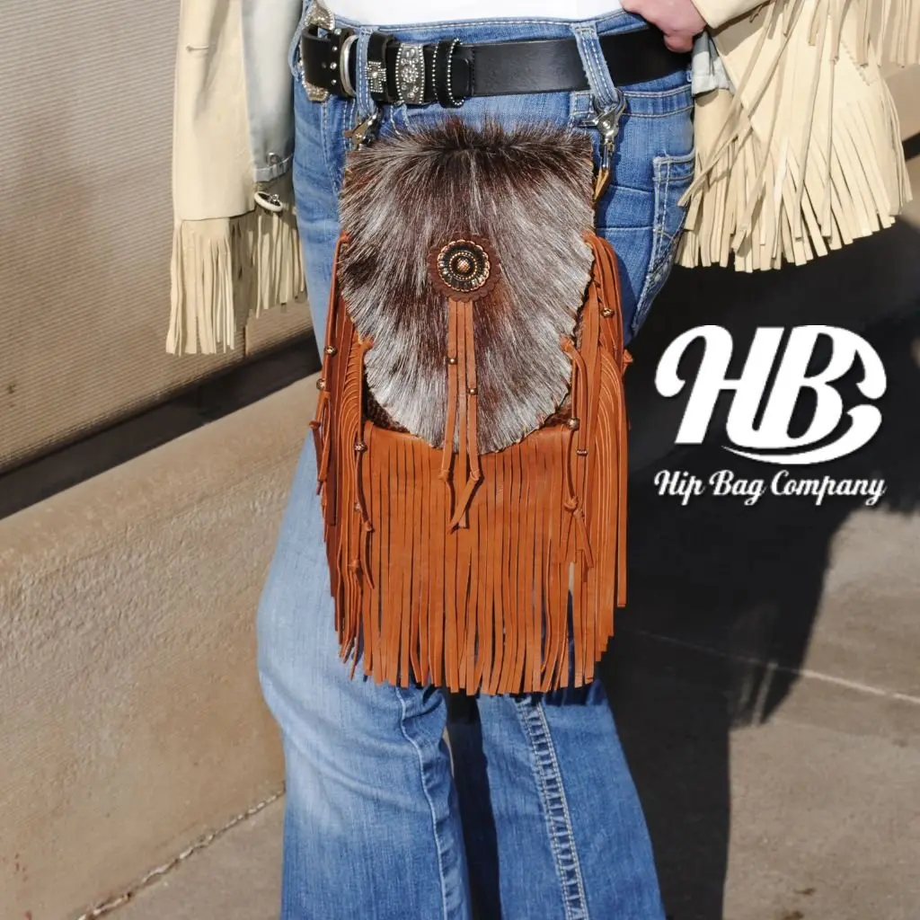 A brown and cream leather hip bag with fringe, hanging from a belt.