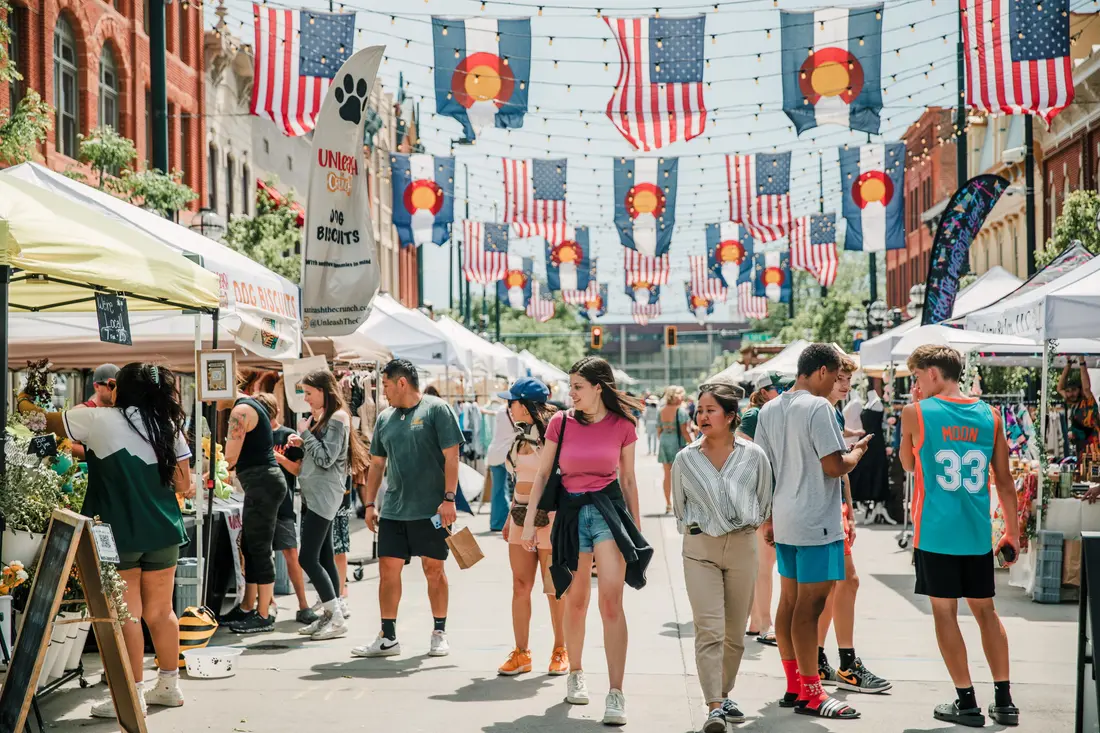 Larimer Square on a market Saturday: shoppers walking the block between white tents under the flag canopy.