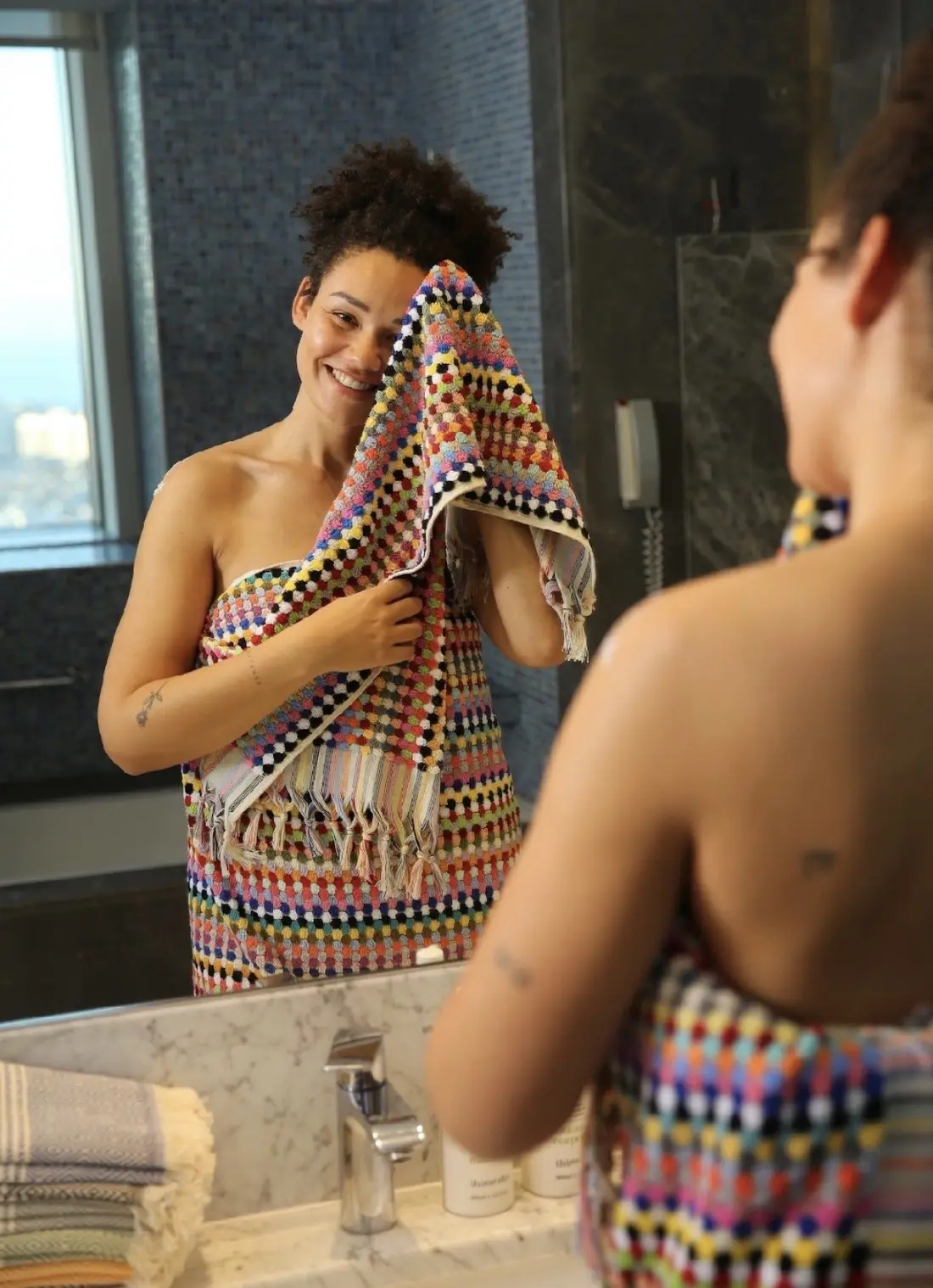 A woman drying off with a patterned Turkish towel at a marble sink.