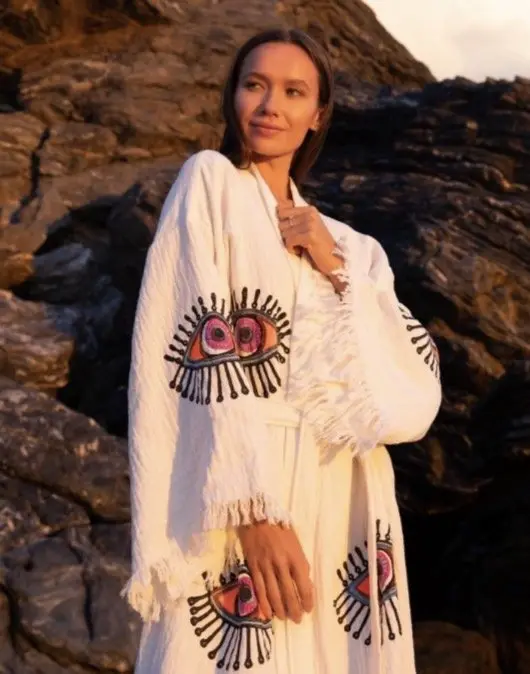 A woman in a white robe with an embroidered evil eye, sitting on red rocks.