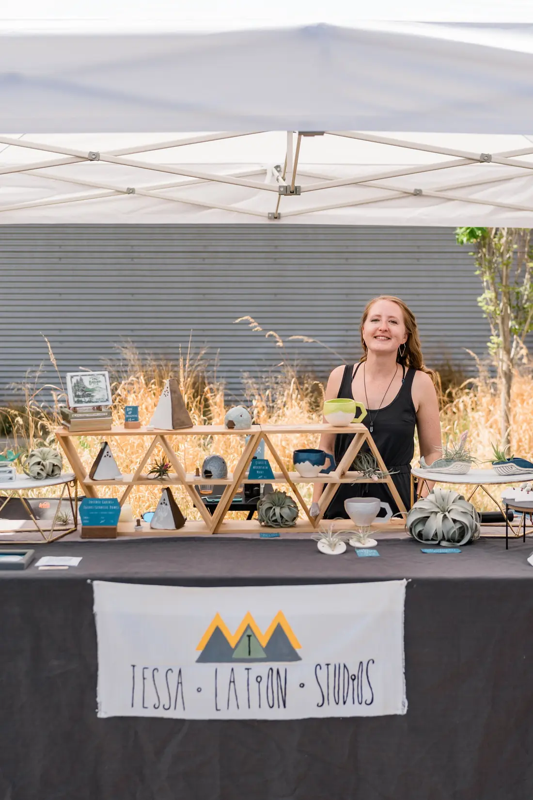 A maker smiling behind her table of ceramics under a white tent at the RiNo Spring BAZAAR.