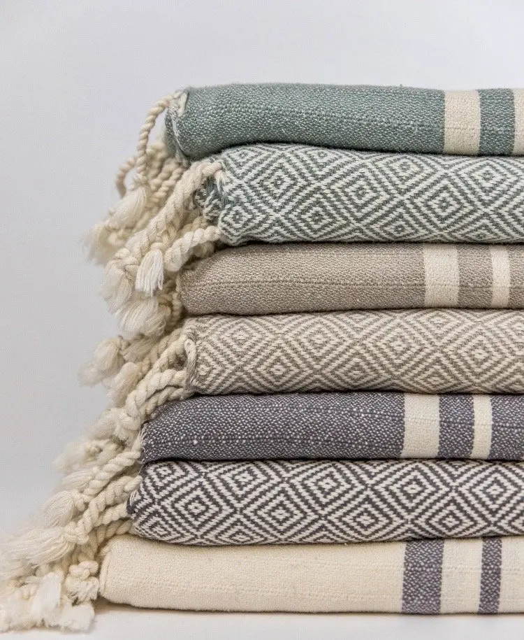 A stack of folded Turkish towels in gray, sage and cream with fringed ends.