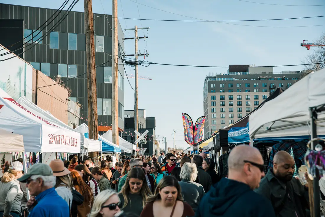 The crowd shoulder to shoulder in the late sun at the RiNo Holiday BAZAAR, tote bags and coffee cups.