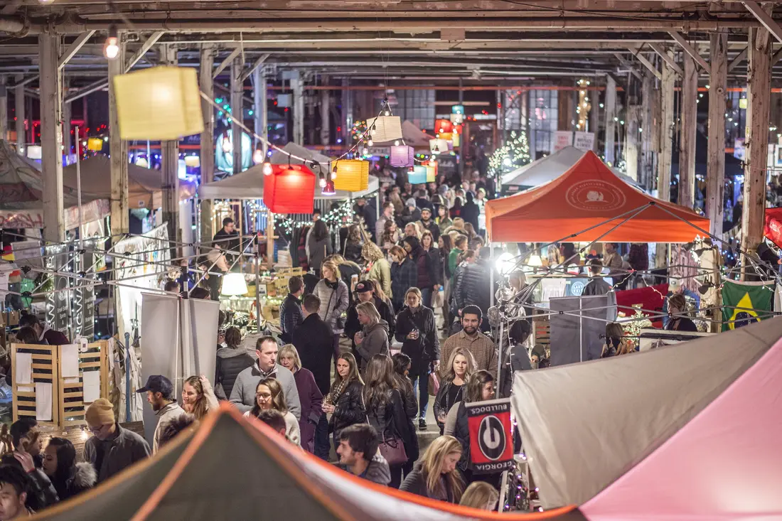 A crowd between tents under hanging lamps at an indoor night market in December 2017.