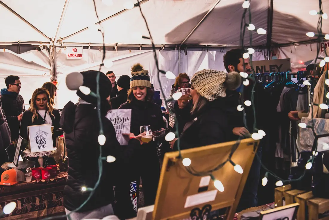 A tent strung with lights at the RiNo Holiday BAZAAR in 2018, makers behind the table.