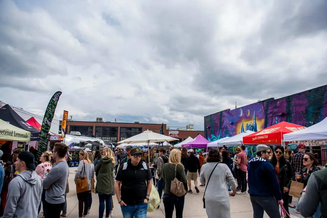 Shoppers walking between tents under a big cloudy sky at the RiNo Spring BAZAAR, 2019, murals behind.