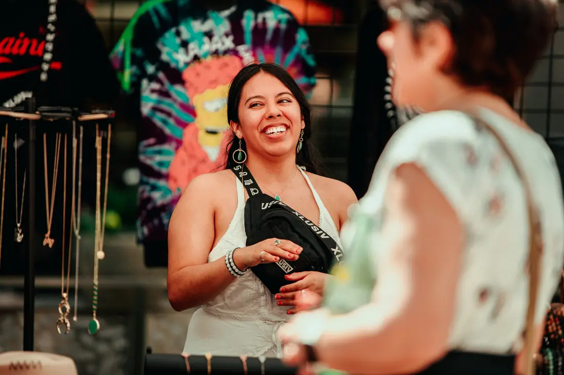 A maker and a shopper laughing across a table at the Belleview Station Spring BAZAAR, May 2021.