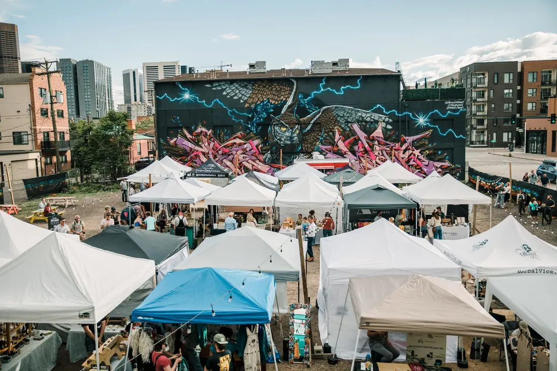 The RiNo Night BAZAAR from above in 2023: rows of white tents in a lot beneath a mural.