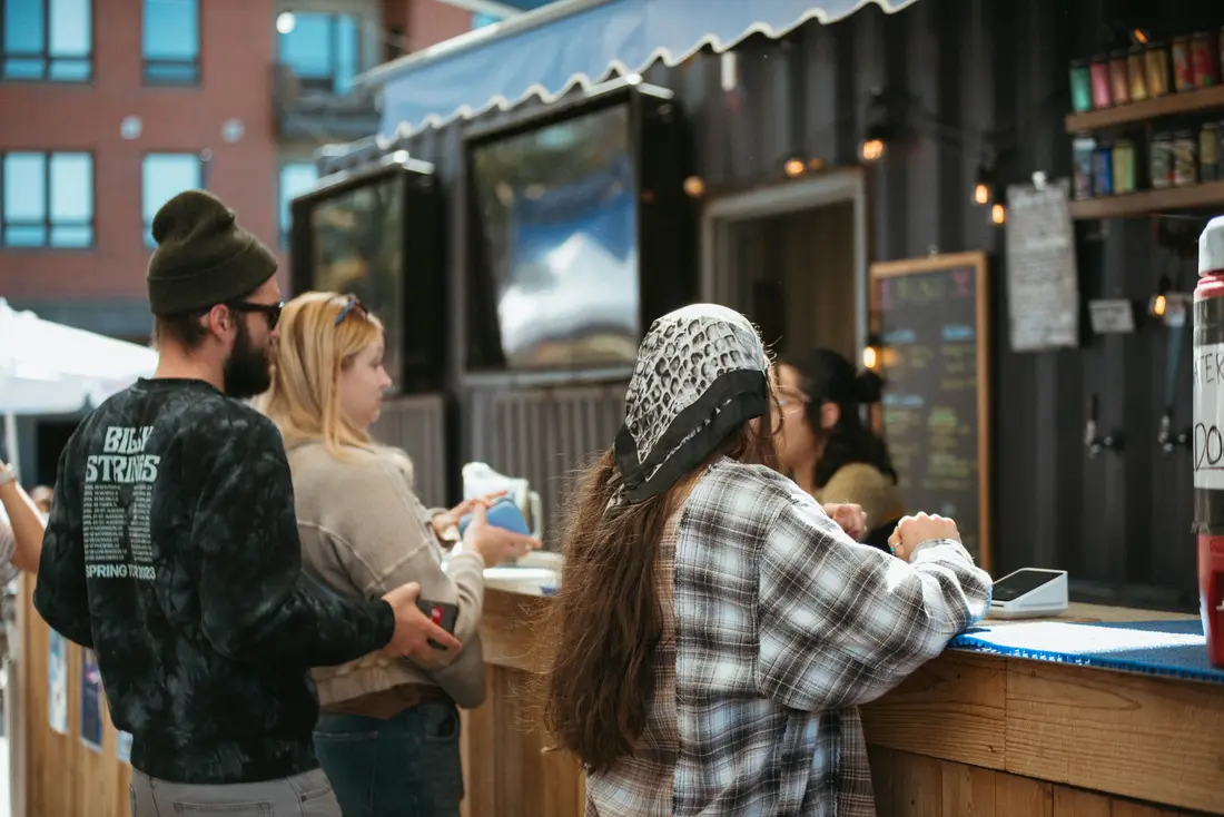 People at the market bar at the Belleview Station Fall BAZAAR, the bartender reaching across the counter.