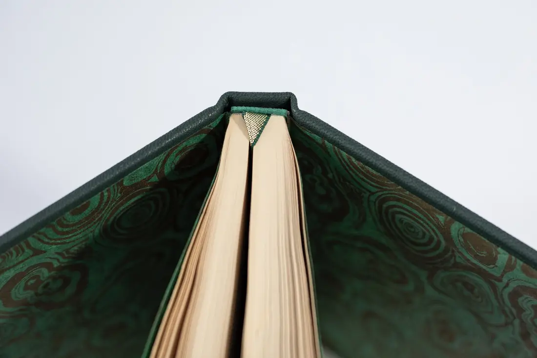 A rebound book standing open, its green patterned endpapers showing.