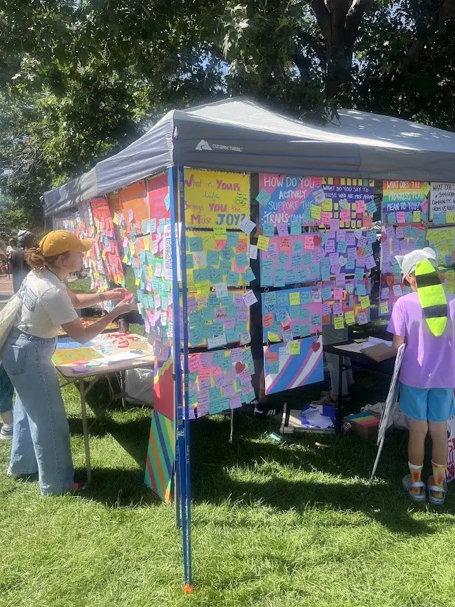 A tent whose walls are covered in sticky notes, children writing at a table beneath.