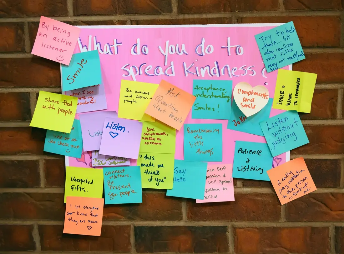 A brick wall covered in colored sticky notes answering the question what do you do to spread kindness.