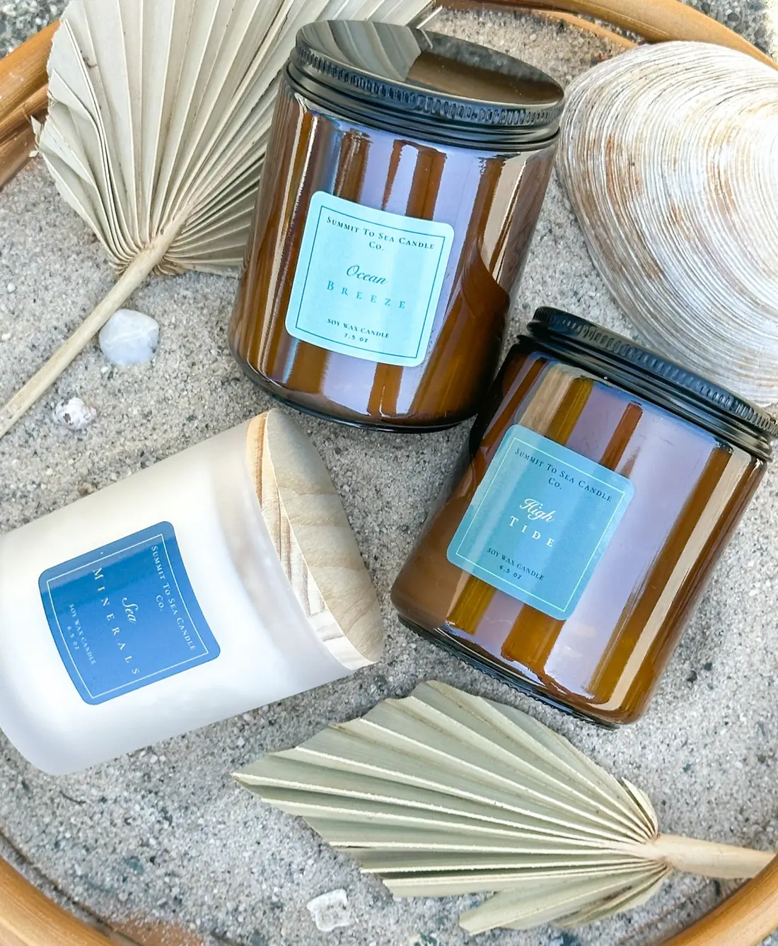 Three amber-glass candles set in sand with dried palm fronds.