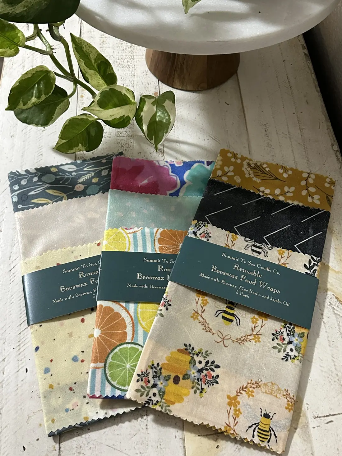 Folded reusable food wraps in fruit and bee prints, fanned out on a cloth.