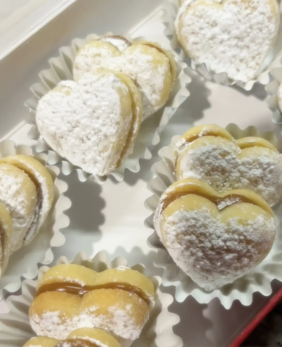 Heart-shaped alfajores dusted with powdered sugar in paper cups.