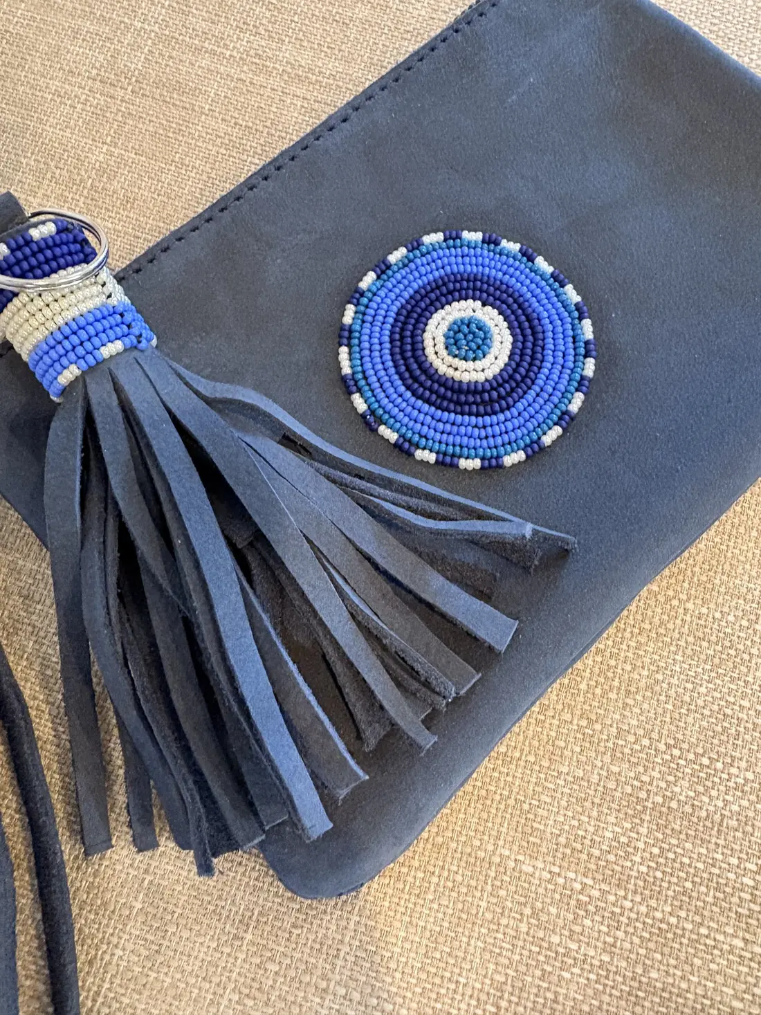 A blue suede pouch with a hand-beaded evil eye and a beaded tassel.