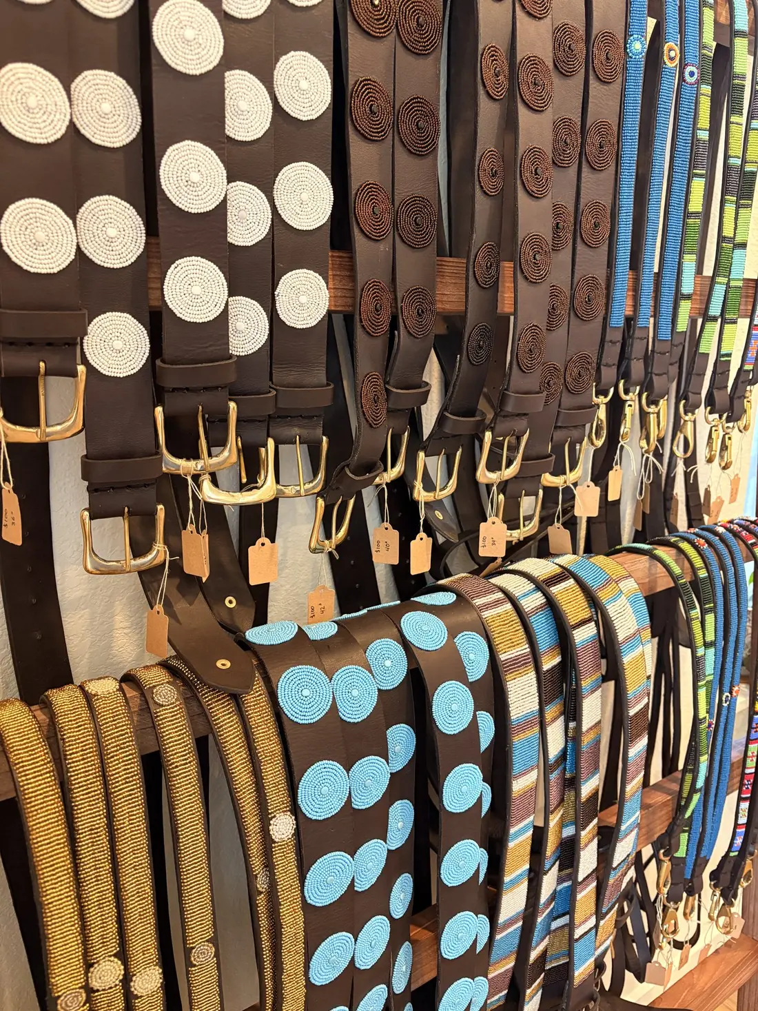 A rack of leather belts with beaded dot patterns in blue, white and brown.