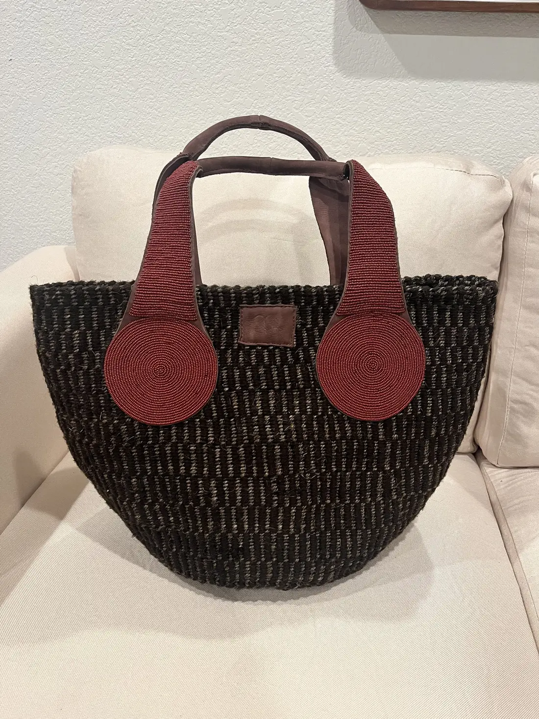 A black woven basket bag with red leather handles on a white chair.